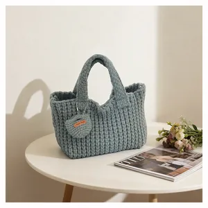 Close-up of gray knitted tote bag texture with 'Hand Made' leather charm tag