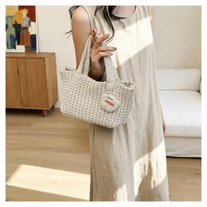 Detail of beige hand-knitted tote bag with 'Hand Made' tag held by a woman