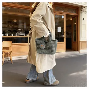Close-up of a dark grey chunky knit handbag with orange tag detail on a beige coat outfit