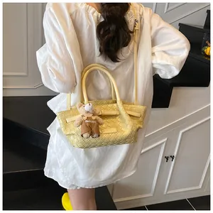 Détail du sac seau jaune tressé avec bandoulière et pendentif ours en peluche mignon