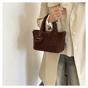 Close-up of hand-made dark brown woven knit bag with a leather tag and square texture
