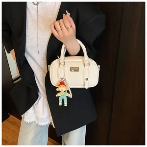 Detail van crème witte PU-leren handtas met metalen logo en een schattige poppenhanger