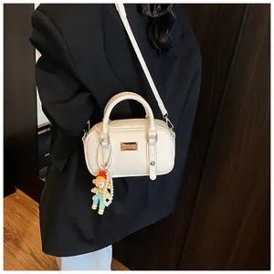 Detail van een crèmewitte handtas met parelpop hanger en verstelbare schouderriem
