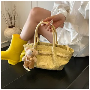 Détail d'un sac seau tressé jaune clair avec une peluche ours mignonne et texture en cuir