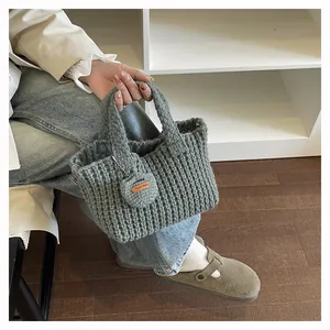 Detail of grey knitted tote bag showing thick wool texture and a brown handmade leather tag