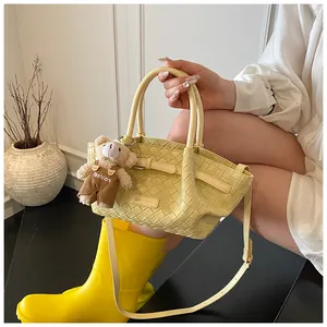 Détail du sac seau tissé jaune clair avec breloque d'ours et longue bandoulière réglable