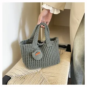 Detail of grey-green knit handbag featuring handmade leather tag and heart charm accessory
