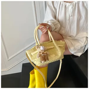 Détail du sac seau tressé jaune avec bandoulière et pendentif ours en peluche mignon