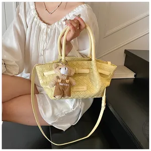 Détail du sac seau tissé jaune avec logo de marque, bandoulière et charmant petit ours