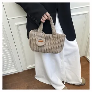 Detail of woven khaki knit tote bag featuring a leather Hand Made logo and round charm