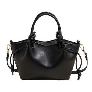 Fashionable black faux leather bucket bag with knot detail and gold hardware on white background