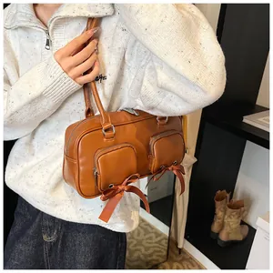 Detail of caramel leather Boston bag featuring zip pockets and decorative ribbon bows