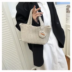 Close-up of oatmeal knit handbag featuring hand-made leather label and heart charm