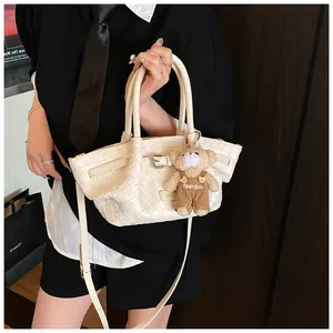 Détail du sac seau tressé crème avec pendentif ours en peluche et bandoulière réglable