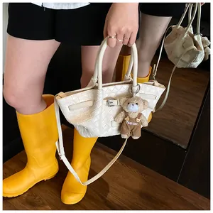 Détail d'un sac seau tissé blanc avec un charm d'ours et texture en similicuir tressé