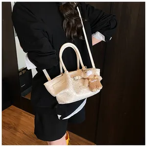 Détail d'un sac seau tressé crème avec pendentif ours et bandoulière réglable