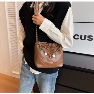 Détail d'un sac seau matelassé marron avec bandoulière en chaîne cuir et breloques émaillées