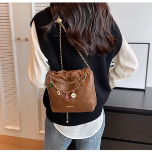 Détail d'un sac seau matelassé marron avec chaîne dorée et breloques de cœur sur un modèle