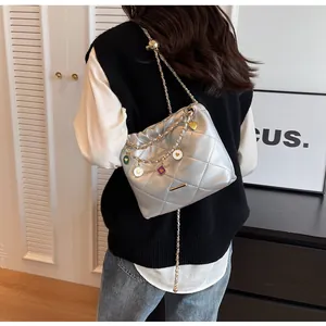 Détail du sac seau argenté matelassé avec chaîne dorée et pendentifs émaillés