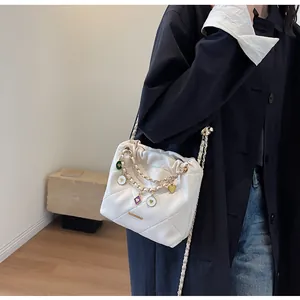 Détails d'un sac seau blanc matelassé avec chaîne dorée et breloques en cœur