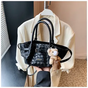 Détail d'un sac seau noir tressé avec plaque métallique et pendentif ours mignon