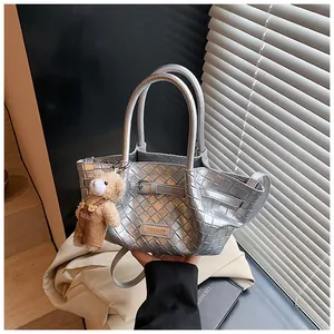 Détail d'un sac seau tressé argenté au fini métallique avec charmant ours peluche