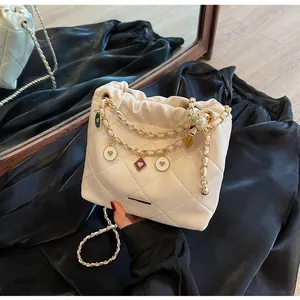 Détail du sac seau matelassé beige avec chaîne dorée et breloques en émail colorées