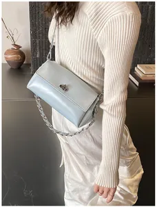 Sac bandoulière bleu clair avec chaîne argentée porté par un mannequin sur fond gris