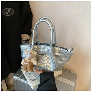 Détail du sac seau tressé argenté avec plaque logo en métal et breloque ours