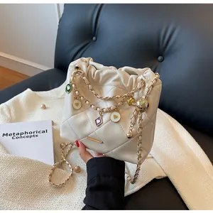 Détails du sac seau crème matelassé avec chaîne dorée et breloques en émail coloré