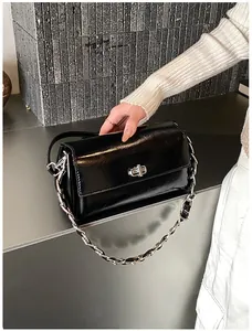 Détail d'un sac en cuir noir brillant avec fermoir rotatif argenté et bandoulière