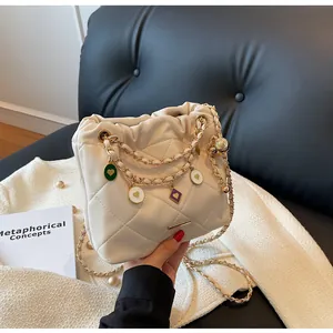 Détail du sac seau matelassé crème avec chaînes dorées décoratives et breloques en cœur