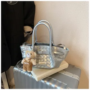 Gros plan du sac seau tressé argenté avec breloque ours et plaque logo de marque