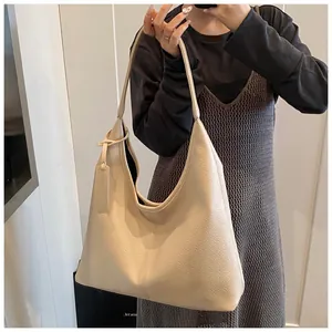 Gros plan d'un grand sac cabas beige en cuir grainé porté par un mannequin au style épuré
