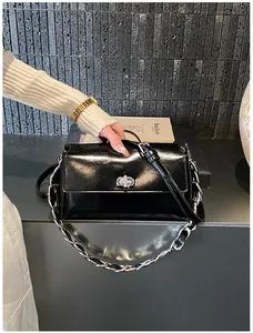 Détail du sac baguette en cuir verni noir avec fermoir argenté et bandoulière chaîne