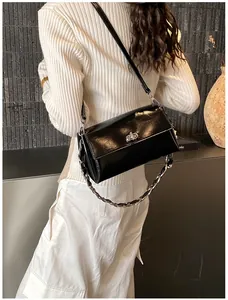 Détail d'un sac bandoulière en cuir verni noir avec un fermoir tournant argenté