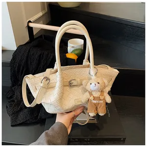 Détail du sac seau tissé crème avec boucle en métal et accessoire de charme ours en peluche