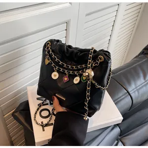Détail d'un sac seau en cuir matelassé noir avec chaînes dorées et breloques cœur