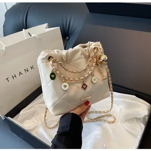 Détail d'un sac seau matelassé crème avec chaîne dorée et breloques en émail coloré