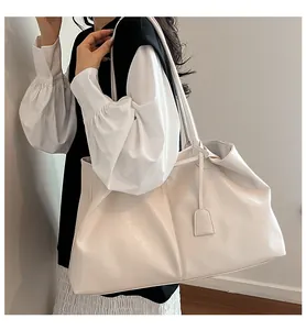 Model wearing a large cream tote bag with slim shoulder straps and a simple pendant