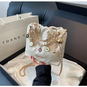 Détail du sac seau matelassé beige avec chaîne dorée et breloques cœur près du coffret