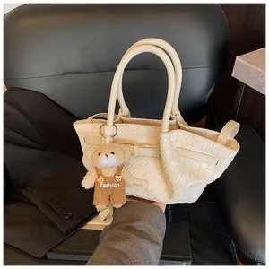 Gros plan d'un sac seau tressé beige avec un pendentif ours et une plaque de marque