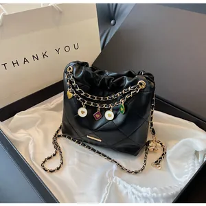 Détail d'un sac seau matelassé avec chaîne dorée et breloques dans une boîte cadeau