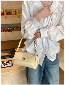 Gros plan du sac beige en cuir verni avec bandoulière chaîne argentée et fermoir rotatif