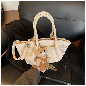 Détail de la texture tressée du sac seau crème avec un pendentif ours sur un siège cuir