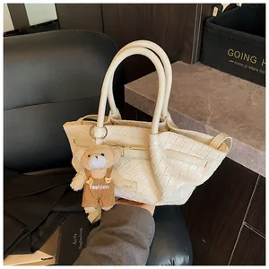 Détail du sac seau en cuir tressé crème avec un adorable accessoire de charme ours en peluche