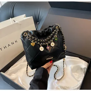 Vue détaillée du sac seau matelassé noir avec chaînes dorées et breloques en coffret cadeau