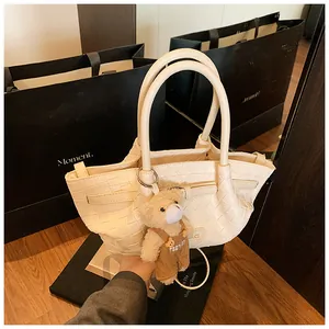 Détail d'un sac seau tressé crème avec pendentif ours en peluche et poignées rondes