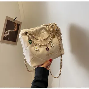 Détail du sac seau matelassé crème avec chaîne dorée et breloques cœurs émaillés