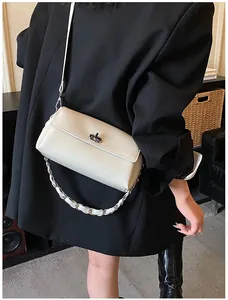 Détail du sac à rabat blanc crème avec fermoir rotatif argenté sur un blazer noir chic